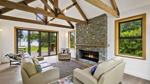 A spacious living room with a stone fireplace, large windows, and a view of the outdoors. - Lakeside Bliss Homestead with outdoor spa (Closeburn)