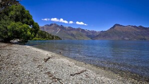 Un lac aux eaux limpides, bordé d’une plage de galets, avec des montagnes en arrière-plan.