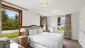 Une chambre à coucher avec un grand lit, deux tables de chevet, une commode, une lampe et une vue sur l’extérieur par une fenêtre.