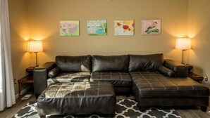 A living room with a sectional sofa, two side tables, and three wall-mounted paintings.