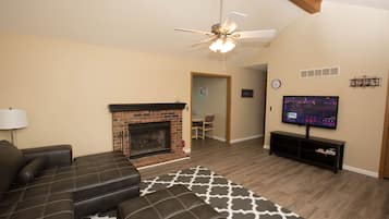 A living room with a fireplace, leather sofa, TV, and a ceiling fan.