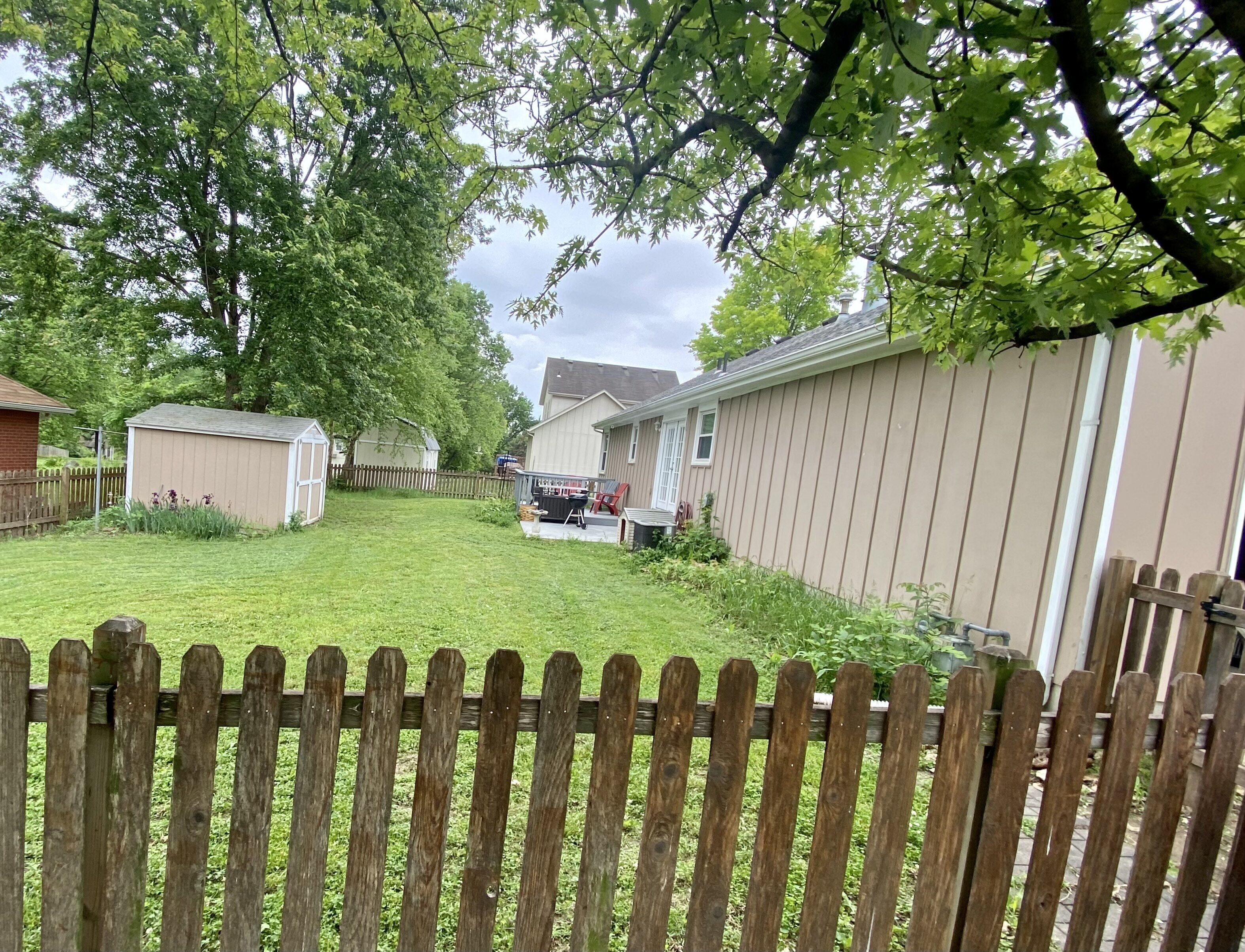 A residential backyard with a wooden fence, a shed, and a house with a covered patio.