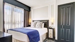 Una habitación de hotel con cama, mesita de noche, lámpara y una puerta.