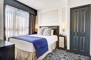 A hotel room with a bed, bedside table, lamp, and a door.