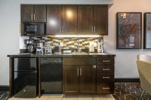 A modern kitchen with dark wood cabinets, a black refrigerator, a microwave, and a tiled backsplash.