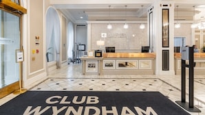 Un área de recepción con mostrador, una araña y un letrero de 'CLUB WYNDHAM' en el suelo.