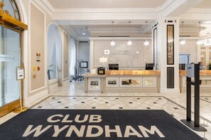 Ein Empfangsbereich mit einer Rezeption, einer Kristallleuchtre und einem 'CLUB WYNDHAM'-Schild am Boden.