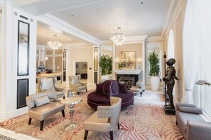 A spacious living area with a plush sofa, armchairs, and a coffee table. A fireplace and a statue are visible in the background.