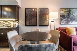 Una sala de estar moderna con una mesa redonda, dos sillas, un sofá y pinturas abstractas en la pared.