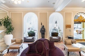 A hotel lobby with a plush seating area, large windows, and a statue.