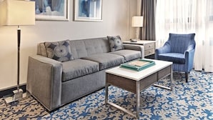 Habitación de hotel con sofá gris, un sillón a juego, una mesita, alfombra estampada y dos cuadros en la pared.