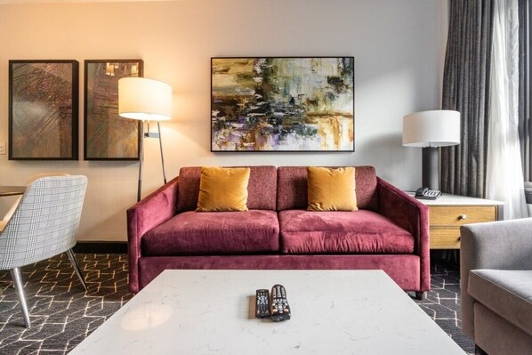 A hotel room with a red sofa, two lamps, a coffee table, and two remote controls.