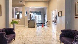 Un vestíbul d'hotel amb un sòl de marbre, dues butaques morades, una recepció i una porta de vidre que dona a una altra sala.