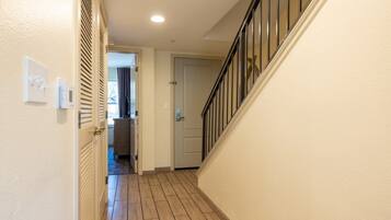 A hallway with a wooden floor, a door at the end, and a staircase with a black railing.