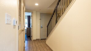 A hallway with a wooden floor, a door at the end, and a staircase with a black railing. - Angels Camp | Friends & Family Golf Getaway | Pool + Golf | 3BR Sleeps 8 (Angels Camp)
