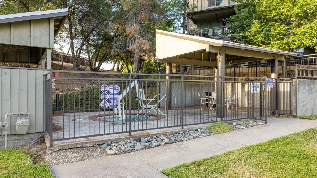 A fenced outdoor area with a covered seating area, a playground, and a building with a flat roof.