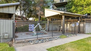 Un espacio al aire libre cercado con una zona de estar cubierta, un parque infantil y un edificio de techo plano.