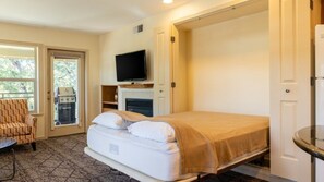 A room with a bed, a television, a fireplace, and a door leading to an outdoor area. - Angels Camp | Friends & Family Golf Getaway | Pool + Golf | 3BR Sleeps 8 (Angels Camp)