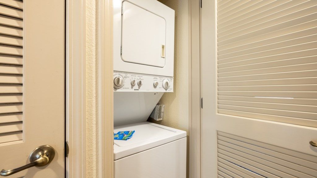 Une buanderie équipée d’un lave-linge et d’un sèche-linge, une porte avec une poignée et une fenêtre avec des stores.
