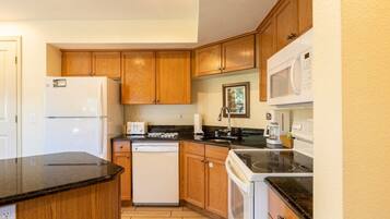 A compact kitchen with wooden cabinets, a white refrigerator, a dishwasher, a microwave, and a stove.