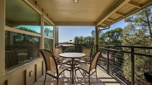 A covered balcony with a table and chairs, large windows, and a view of trees and buildings.