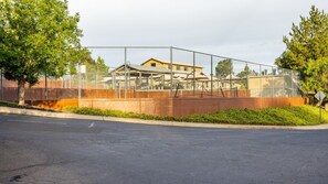 A fenced tennis court area with a building in the background. - Angels Camp | Friends & Family Golf Getaway | Pool + Golf | 3BR Sleeps 8 (Angels Camp)