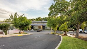 A parking lot with several cars, a building with a flat roof, and trees. - Angels Camp | Friends & Family Golf Getaway | Pool + Golf | 3BR Sleeps 8 (Angels Camp)