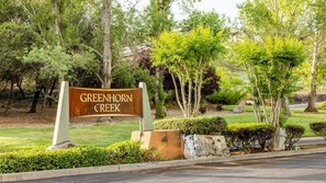 Señal de Greenhorn Creek con un área ajardinada que incluye árboles y arbustos.