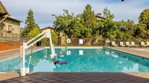 Una piscina con trampolín, rodeada de árboles y un área cercada con sillas de descanso.