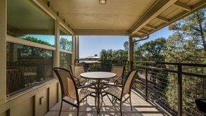Een balkon met overkapping, een tafel, stoelen, grote ramen en uitzicht op bomen en gebouwen.