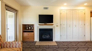 A living room with a fireplace, a television mounted above it, a set of white doors, and a patterned carpet. - Angels Camp | Friends & Family Golf Getaway | Pool + Golf | 3BR Sleeps 8 (Angels Camp)
