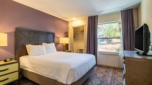 A hotel room with a large bed, bedside tables, a TV, and a window with curtains. - Angels Camp | Friends & Family Golf Getaway | Pool + Golf | 3BR Sleeps 8 (Angels Camp)