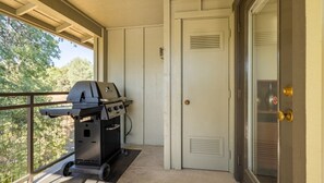 Un balcón con una parrilla, una puerta y vistas a árboles.