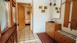Un pasillo con una puerta de madera, una cama pequeña, un aparador de madera con un teléfono y un espejo en la pared.