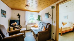 Una sala de estar acogedora con sofá, sillón, televisor y un ventanal con cortinas.
