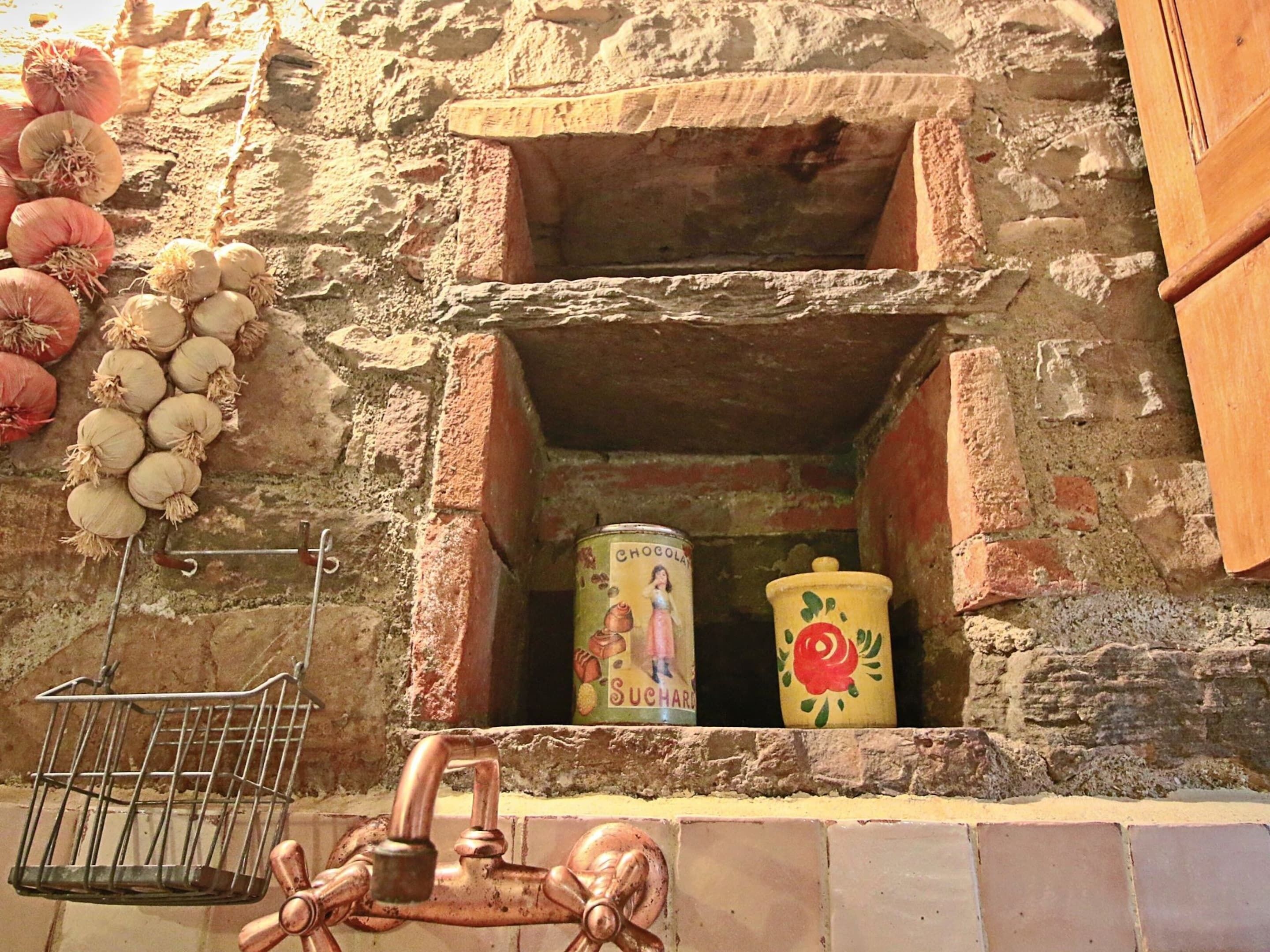 A rustic stone wall with a metal basket, a copper faucet, and two ceramic containers.