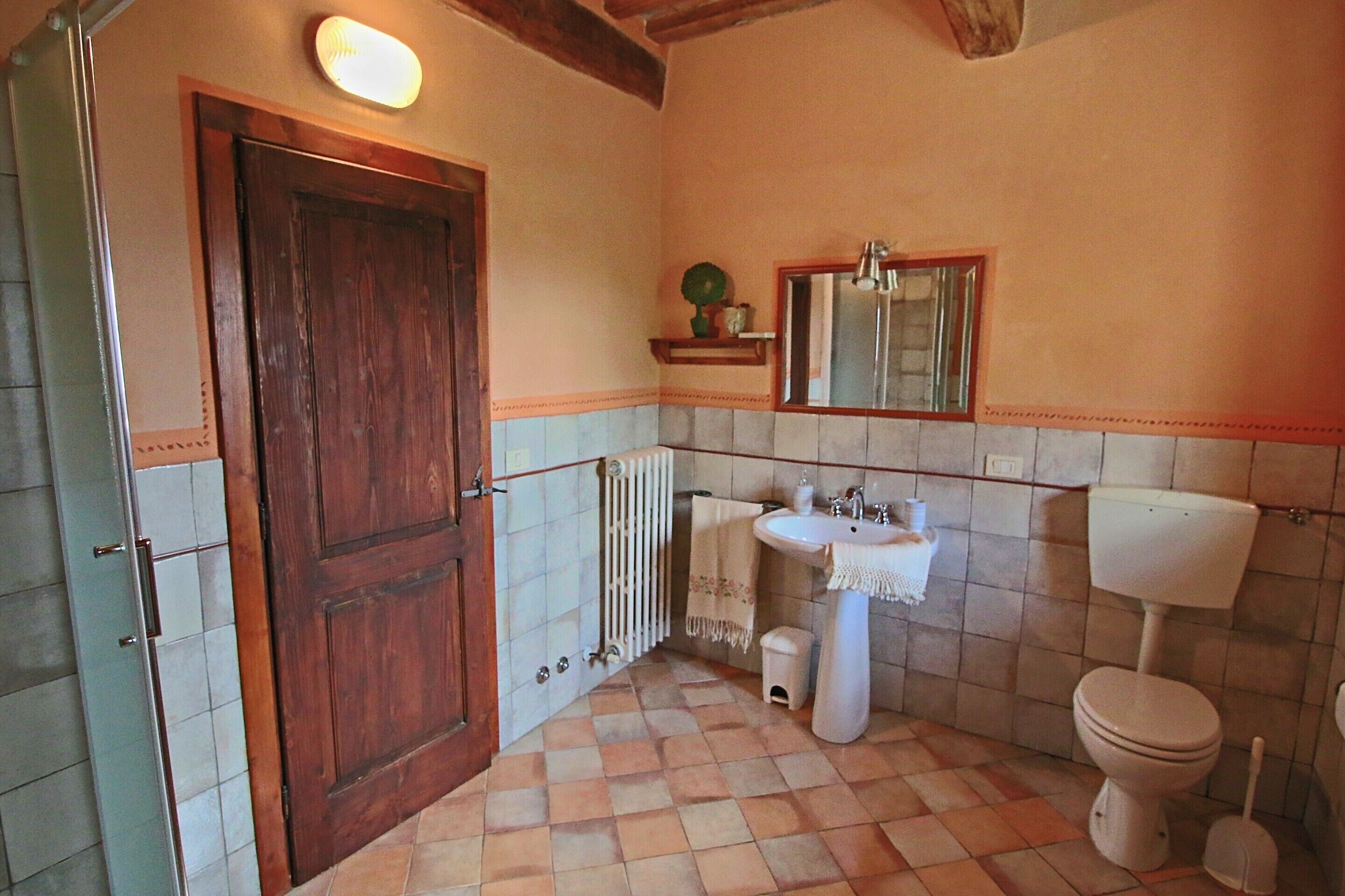 Ein Badezimmer mit Holztür, weißen Fliesen, einem Waschbecken, einer Toilette und einem Spiegel.