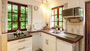 A compact kitchen with white cabinets, a built-in microwave, a kettle, and a sink. - Nature Escape in Bohon (Durbuy)