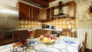 Une cuisine avec des meubles en bois, un mur en pierre et une table dressée avec un panier de fruits, des verres à vin et une bouteille.