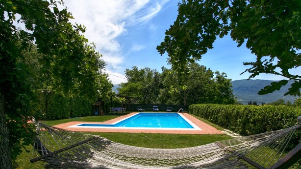 Un hamac installé dans un espace verdoyant, avec une piscine et une vue sur les montagnes en arrière-plan.