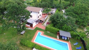 Vue aérienne d’une propriété résidentielle dotée d’une piscine, d’un petit abri de jardin et d’un espace clôturé avec des chaises longues.