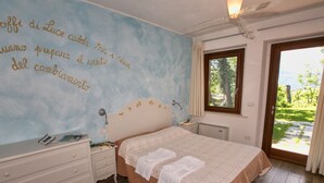 Une chambre à coucher comprenant un lit, une table de chevet, une commode et une fenêtre donnant sur un paysage verdoyant.