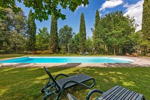Piscina com espreguiçadeiras, cercada por árvores altas e um céu limpo.