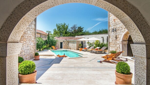 An outdoor swimming pool area with stone walls, lounge chairs, and potted plants. - Holiday Home with Swimming Pool near Lim Bay & Beach (Vrsar)