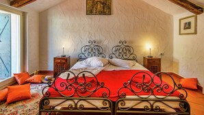 A bedroom with a sloped ceiling, a bed with ornate metal headboard, two bedside tables with lamps, and a window with a view. - Holiday Home with Swimming Pool near Lim Bay & Beach (Vrsar)