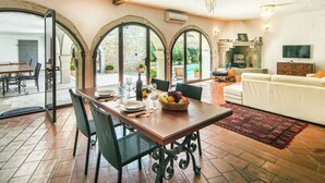 A spacious living area with a dining table, chairs, and a sofa. There are large windows and a TV mounted on the wall. - Holiday Home with Swimming Pool near Lim Bay & Beach (Vrsar)