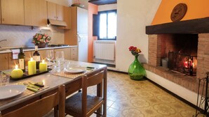 A cozy kitchen with wooden cabinets, a dining table set for two, a vase with flowers, and a fireplace. - Farmhouse in Dicomano With Tuscan Views (Dicomano)
