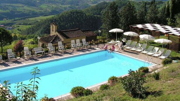 A pool with lounge chairs and umbrellas, surrounded by greenery and hills. - Farmhouse in Dicomano With Tuscan Views (Dicomano)
