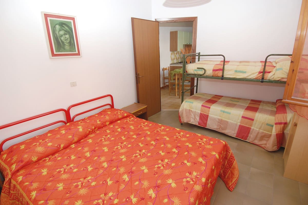 A small, well-lit room with a single bed, a bunk bed, and a desk.