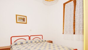 A single bed with a checkered bedspread, a wooden nightstand, a small table, and a wall-mounted picture. - Sun Drenched Seaside Holiday Home near Venice (Rosolina)